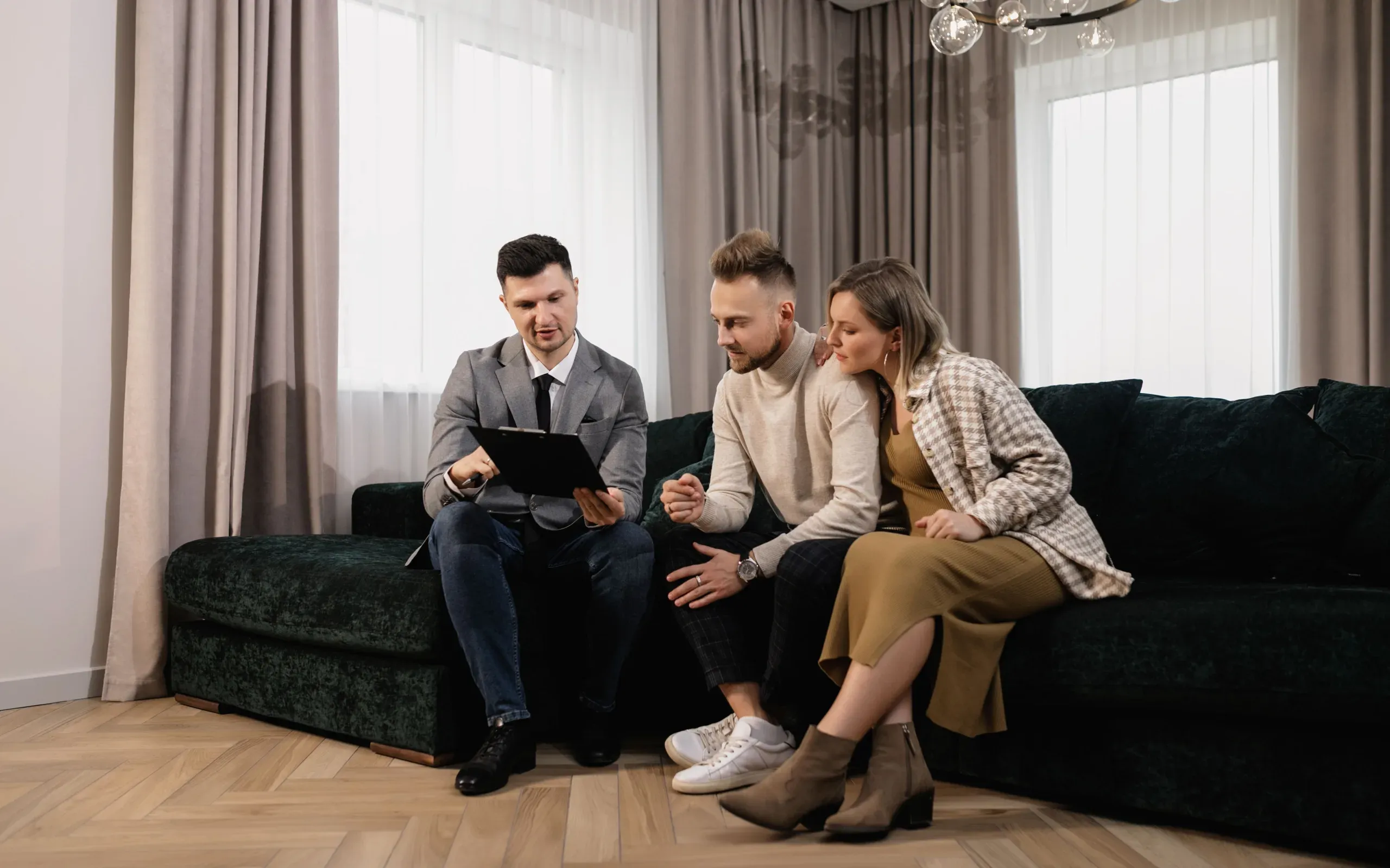 Un agent immobilier présente une annonce sur tablette à un couple installé dans un salon clair